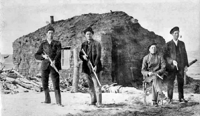 Homesteaders at Strool, South Dakota, 1909. Four men in front of a sod house, each holding a rifle or gun. 